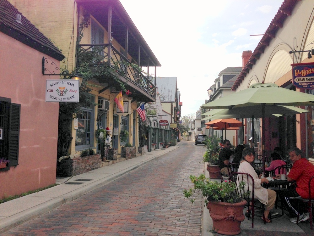 Saint Augustine city street with people eating outdoors under umbrellas and colorful storefronts